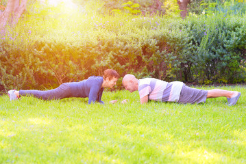 Active seniors makes plank in autumn nature. Happy old couple relax outdoor in Summer day. Workout, sports, sports training, fitness for elderly people concept..