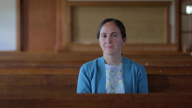 A portrait of a young Mennonite woman sitting in an empty church.