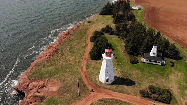 Lighthouse by the seashore, tourists taking pictures and walking to their cars