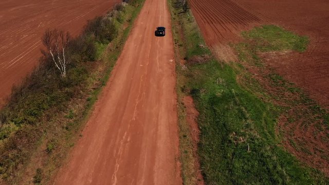Black car driving along a red dirt road in the country