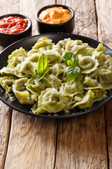 Boiled spinach green cappelletti, ravioli, tortellini stuffed with meat with parmesan cheese and basil served with sauces close-up. vertical