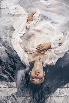 close up portrait of beautiful woman lying in water with fabric. Fashion concept