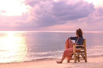 beautiful young woman sitting in chair on the beach at sunset - Powered by Adobe