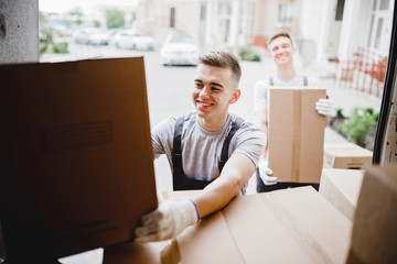 A young handsome smiling mover wearing uniform is reaching for the box while unloading the van full of boxes. House move, mover service.