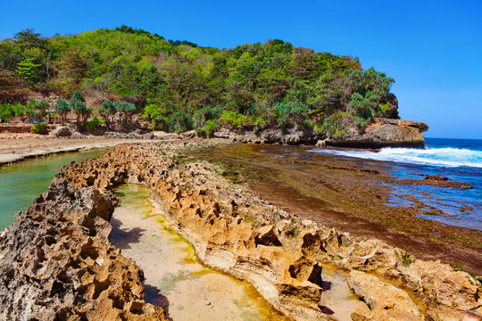 Popular travel destination in East Java - Pantai Batu Bengkung beach with calm water lagoon separated from sea surf by reef barrier. Scenic view of natural swimming pool. Family vacation in Indonesia.