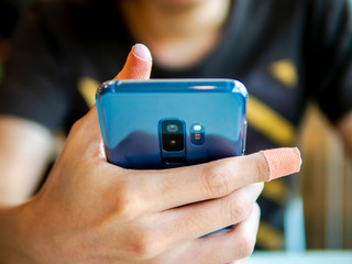 close up of a man injured have plaster on thumb and index finger holding smart phone. for browsing, searching, reading, work or selecting help by call an ambulance, insurance health, hospital