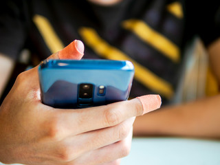 man injured have plaster on thumb and index finger holding smart phone. for browsing, searching, reading, work or selecting help by call an ambulance, insurance health, hospital by mobile app concept.