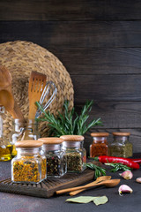 Products for cooking in kitchen, kitchen utensils, herbs, colorful dry spices in glass jars on dark background