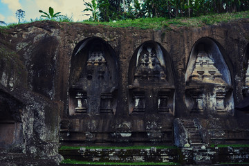 Fototapeta na wymiar Beautiful view of ancient stone carving of temple on Bali island. Gunung Kawi Temple and Candi in jungle at Bali, Indonesia. Old temples in the jungle. Ancient temple ruins. Carved in stone temple.