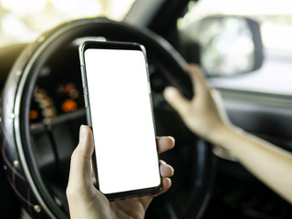 Driver use smart phone while driving. white screen for mock up, graphic design or application promotion. Steering wheel interior right-hand drive car in background.