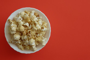 Popcorn in a white ceramic bowl on an orange background. View from above.