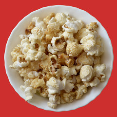 Popcorn in a white ceramic bowl on an orange background. Top view, square.Isolate.