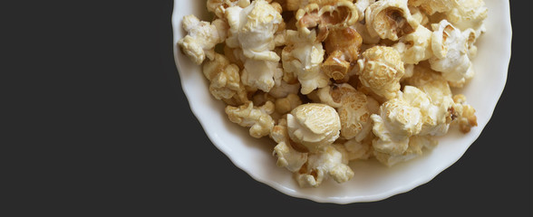 Popcorn in a white ceramic bowl on a dark gray background. Top view, horizontal banner. Isolate.