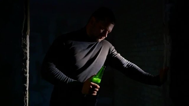 drunk alcoholic man standing in a ruined building in the dark and drinking beer from a bottle