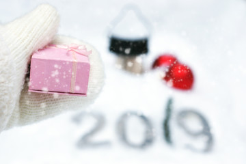A gift for the new year 2019, a hand in a white knitted mitten stretches a pink box.