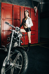 Fototapeta na wymiar Beautiful girl in leather tight fitting clothes on high heels near a bike