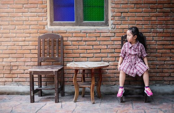Baby girl sitting on a chair in front of red brick wall while waiting for her parent 