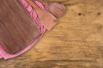 Cutting board and a spoon on a kitchen napkin on old wooden table.