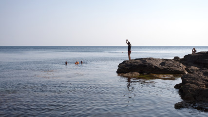Fototapeta na wymiar Tourism. Journeys. Sea. Young man jumping from stone to sea
