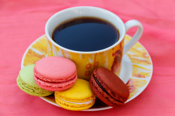 Cup of coffee with tasty colorful macarons on pink background