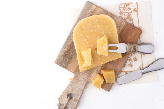 Parmesan cheese, on a wooden board and on a white background a knife for cheese. Traditional food. Free space for text. Top view