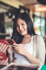 Beautiful attractive young Asian woman using smart phone or cellphone or tablet at cafe in the morning 