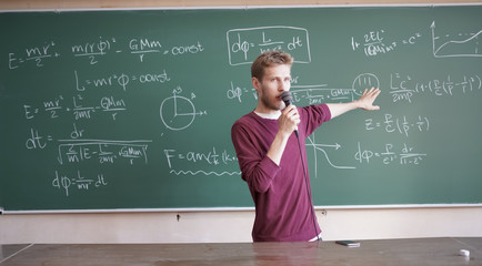 young professor teacher with microphone standing near the blackboard and speaking on the university...