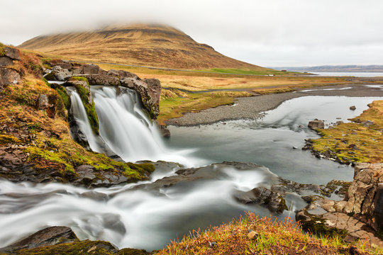 Long exposure photo of Kirkjufellsfoss facing Kirkjufell ("Church Mountain") under partial fog cover. Located near Grundarfjordur in the Western Region of Iceland.