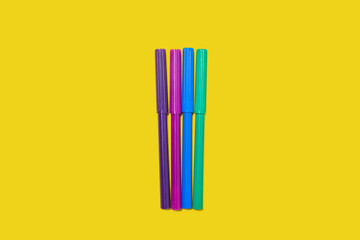 four new bright plastic colored felt pens lying on a yellow background. concept of office supplies