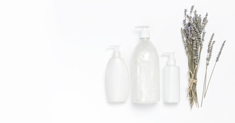 Cosmetic bottle containers with a bouquet of lavender on white background flat lay top view. Blank label for branding mock-up. Natural beauty product concept. Shower gel, shampoo, liquid soap