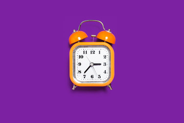 Vintage style orange metal alarm clock with bells standing on the purple surface isolated. back to school concept. free space for text