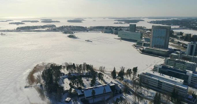 Aerial view, drone flying forward. Office buildings and business district near frozen sea with snow and during sunny day in Helsinki, Espoo, Keilaniemi, Finland