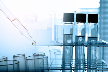 Dropping chemical liquid to test tube with lab glassware background, science or medical research and development concept.