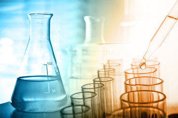 Dropping chemical liquid to test tube with lab glassware background, science or medical research and development concept.