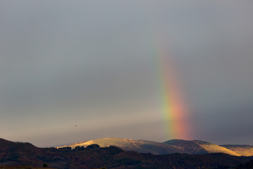 Beautiful and surreal view of part of a rainbow over some hills with birds flying