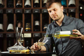 Sommelier pouring white wine from bottle in glass