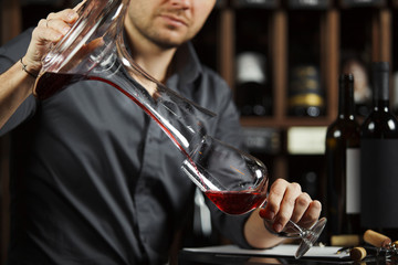 Sommelier pouring wine into glass from mixing bowl. Male waiter