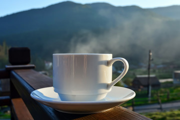 a cup of tea, coffee, standing on the porch of the hotel balcony, overlooking the mountains, in the early morning in the sunlight
