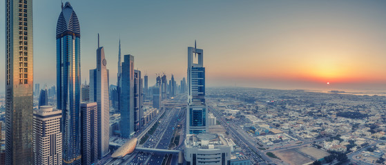 Obraz premium Skyscrapers and highways of a big modern city at sunset. Aerial panoramic view on downtown Dubai, United Arab Emirates.