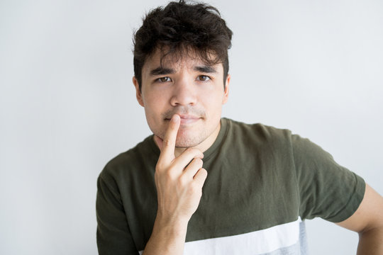 Portrait Of Pensive Young Asian Man Looking At Camera. Vietnamese Guy Standing With Hand On Chin With Thoughtful Expression. Decision Or Doubt Concept