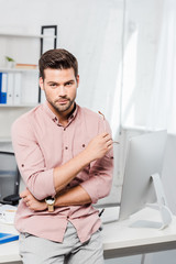 Fototapeta premium handsome young businessman leaning back at workplace and looking at camera