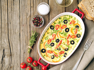 Casserole dish, delicious hot omelette with tomatoes, olives, capsicum. Old wood background, top view, copy space