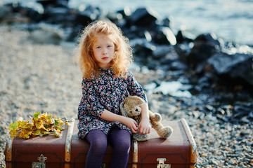Portrait of a sad little girl. Sitting on an old suitcase with h