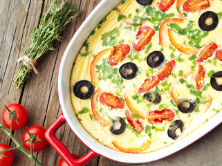 Casserole dish, delicious hot omelette with tomatoes, olives, capsicum. Old wood texture background, top view, close-up