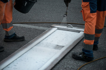 Traffic line painting. Workers are painting white street lines on pedestrian crossing. Road cones with orange and white stripes in background, standing on asphalt during road construction works
