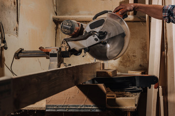 partial view of carpenter using circular saw at wooden workshop