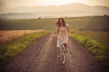 pretty young smilling woman with retro bicycle in sunset on the road, vintage old times, girl in retro style on meadow