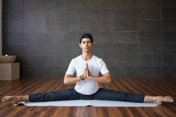 Experienced Indian yogi doing splits in gym. Man looking at camera, holding hands together and...