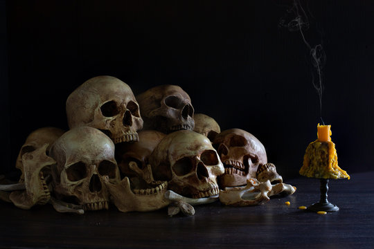 Pile of skulls with bones and Candle which has flame to be bright in the dark light room