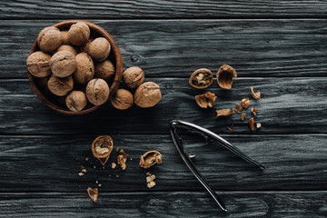walnuts in wooden bowl and nutcracker on dark wooden background
